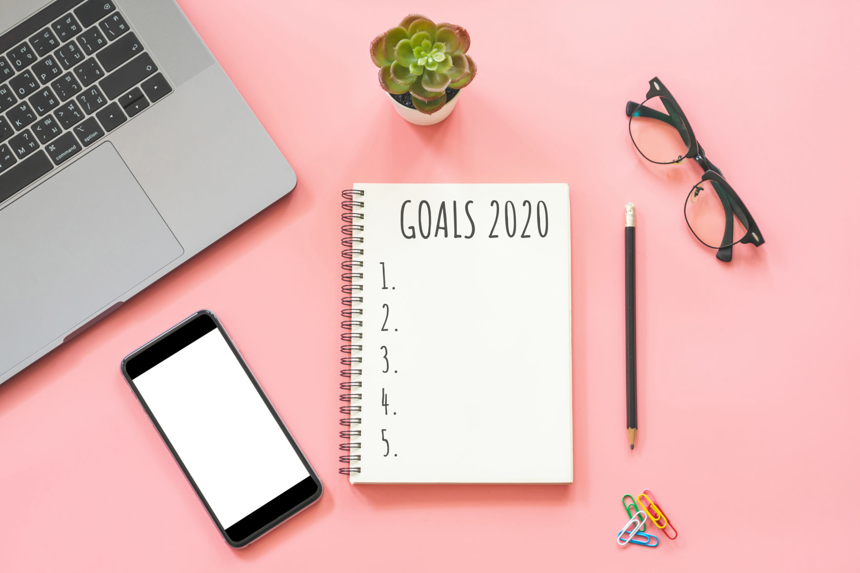 2020 New year concept. Goals list in stationery, laptop, notebook, smartphone, pot plant on pink pastel color with copy space